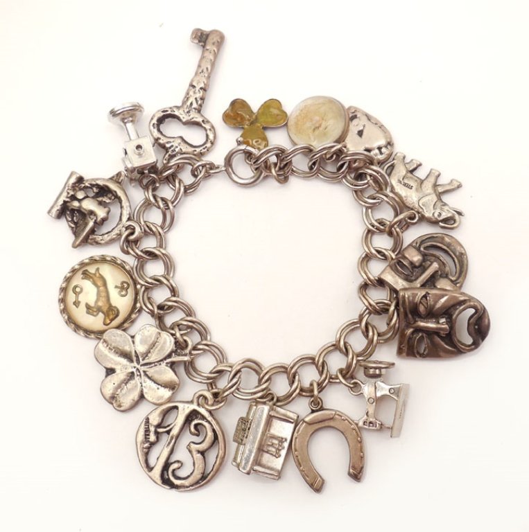 Sterling silver charm bracelet: Sterling silver charm bracelet with fourteen assorted charms including key, movie projector, eagle, ram zodiac sign, four leaf clover, lucky 13, piano, horse shoe, sewing machine, comedy and tragedy,