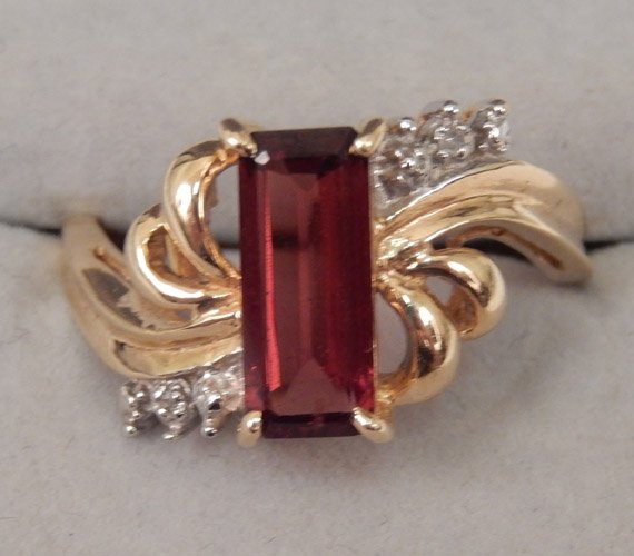 10k gold and garnet ring: 10k gold and garnet ring with diamond accents and ribbon style band, baguette cut stone measures approximately 10mm x 3mm, size 7, stamped 10k, weighs 2.7 gr/1.8 dwt complete, late 20th C.