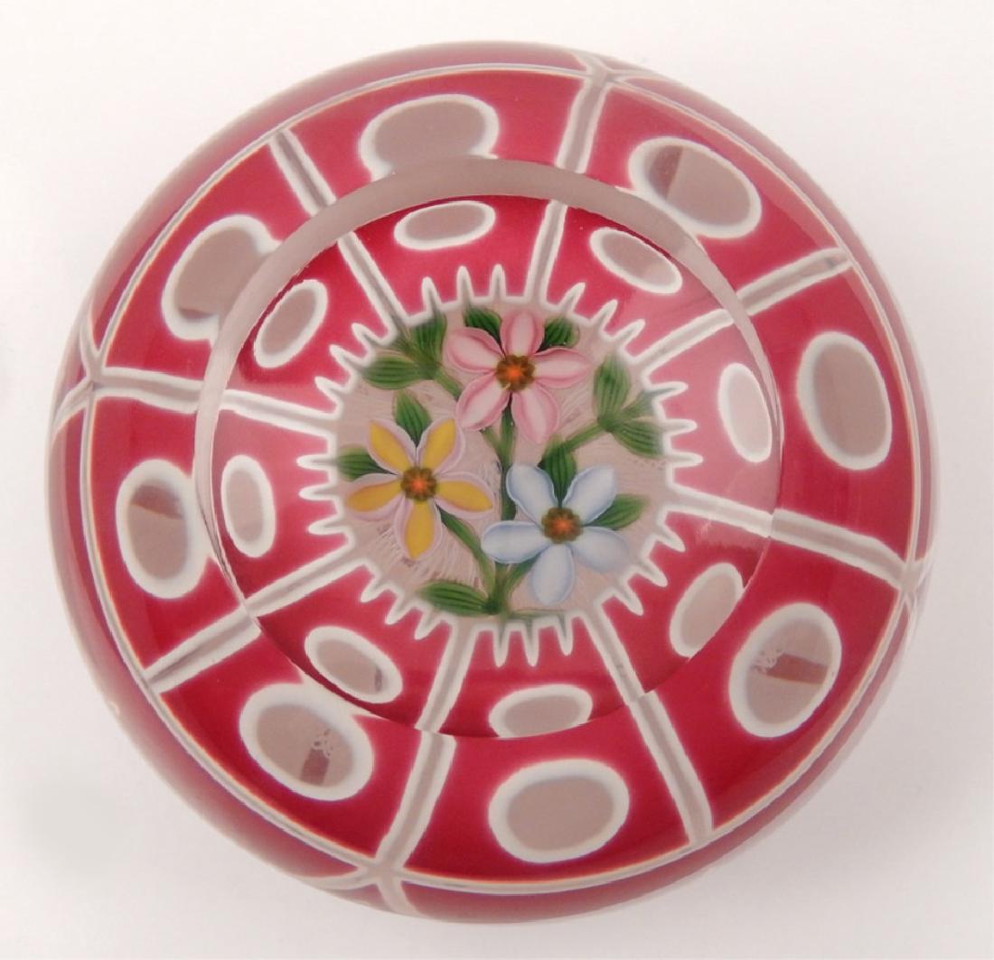 Magnum John Deacons art glass paperweight: Magnum John Deacons art glass paperweight, encased double overlay in hot pink and white with sharks tooth cutting, center has three open flowers, one pink, one yellow, and one blue, surrounded with gr