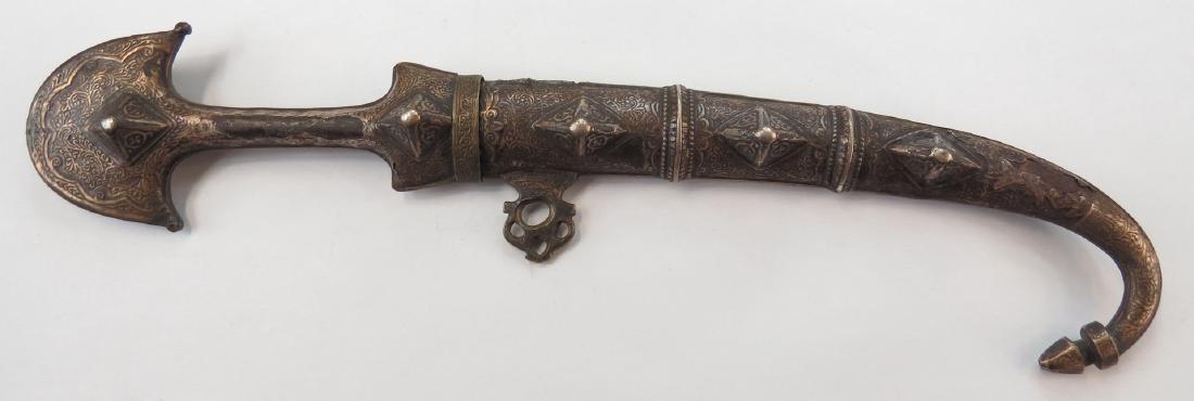 A MOROCCAN KOUMIYYA DAGGER: An older example, mounted in engraved silver, with flared pommel and curved blade, in its matching scabbard. Embellished overall. 19th century. Well worn. Overall length 42 cm. Condition IV