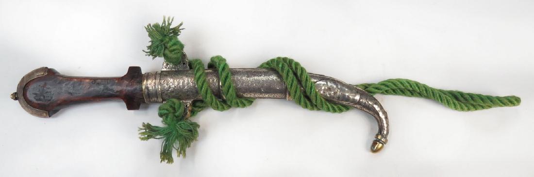A MOROCCAN KOUMIYYA DAGGER: Mounted in engraved silver and brass, with flared pommel and curved blade, in its matching scabbard. Embellished overall. 19th century. Well worn. Overall length 38.5 cm. Condition III
