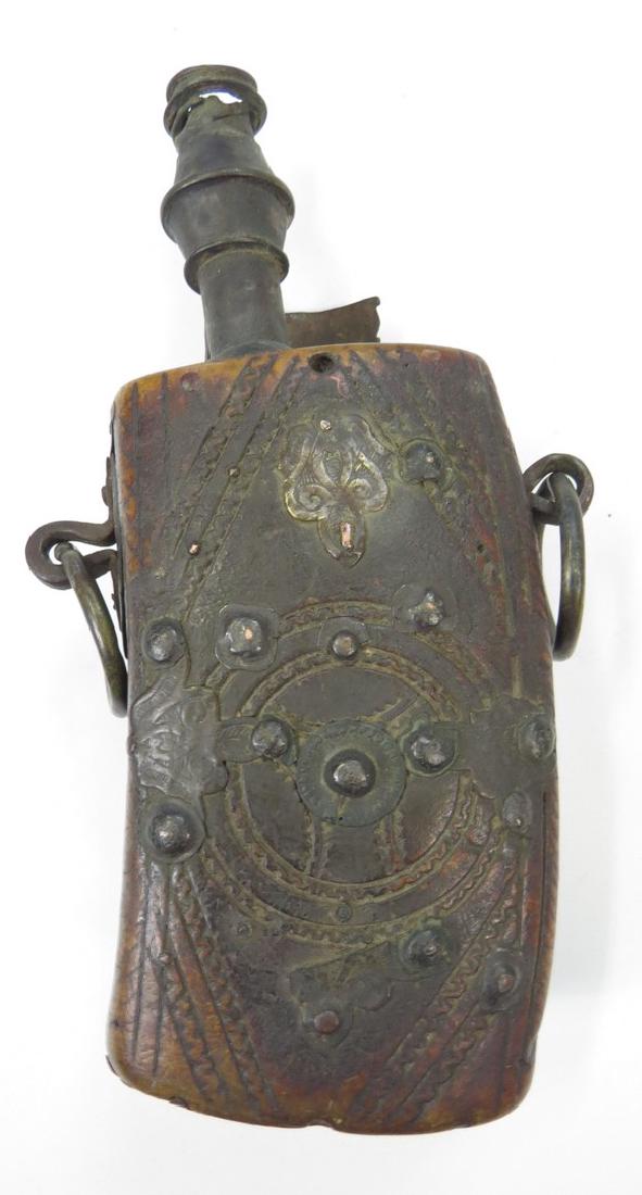 A MOROCCAN POWDER FLASK: A much earlier than average example, closely duplicating its German prototype. Carved of a single section of horn, carved in geometrical motifs overall and set with studs and engraved plates, the bras