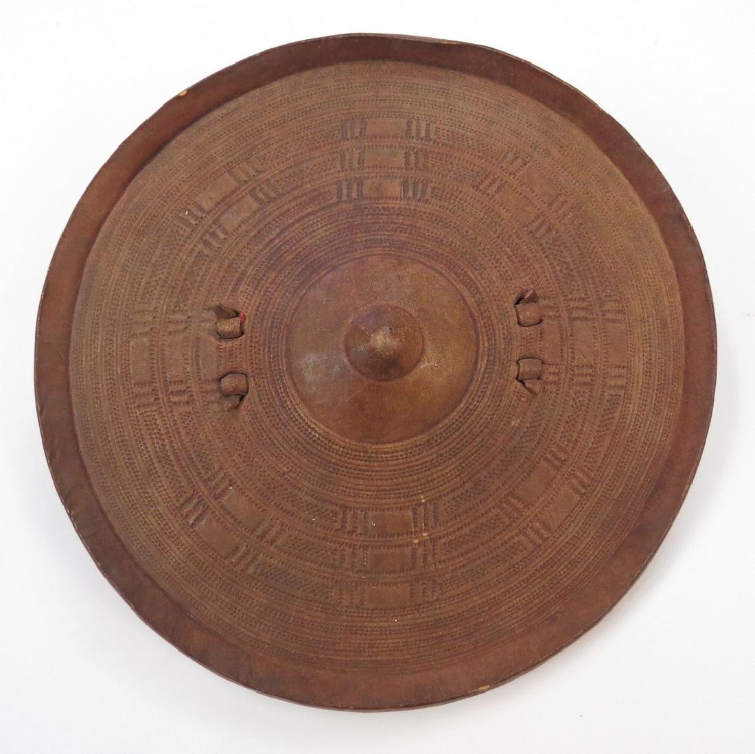 AN ABYSSINIAN SHIELD: Of molded rawhide with separately-applied grip, the surface with characteristic minute geometrical tooled motifs overall. Mid 19th century. Diameter 29.8 cm. Condition I