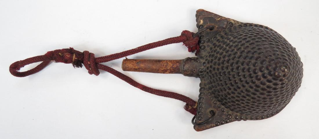 A MOROCCAN POWDER FLASK: The wooden body of characteristic domed form with projecting suspension tabs, covered entirely in leather and heavily embellished with brass studs. Retains its woven cord. First half of the 19th centu