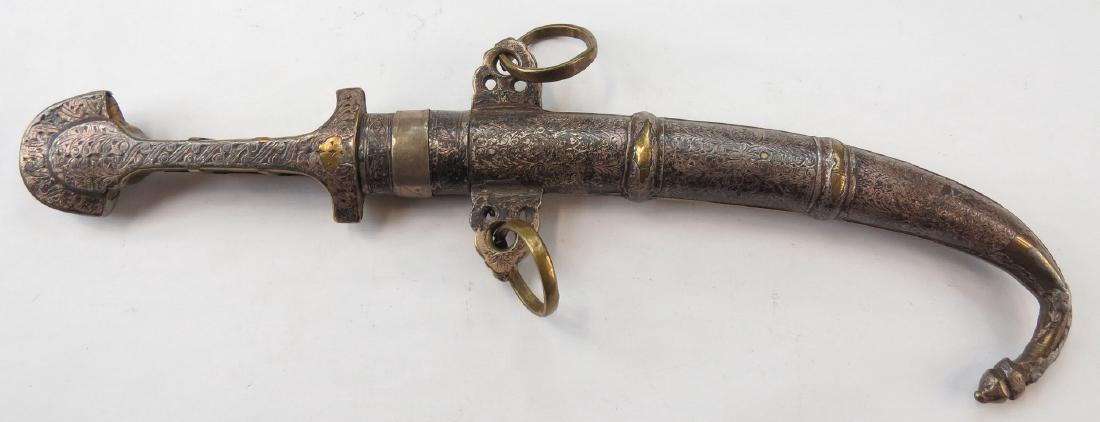 A MOROCCAN KOUMIYYA DAGGER: The grip with flared pommel and curved blade, in its matching silver and brass scabbard. Embellished overall. 19th century. Worn. Overall length 39 cm. Condition III