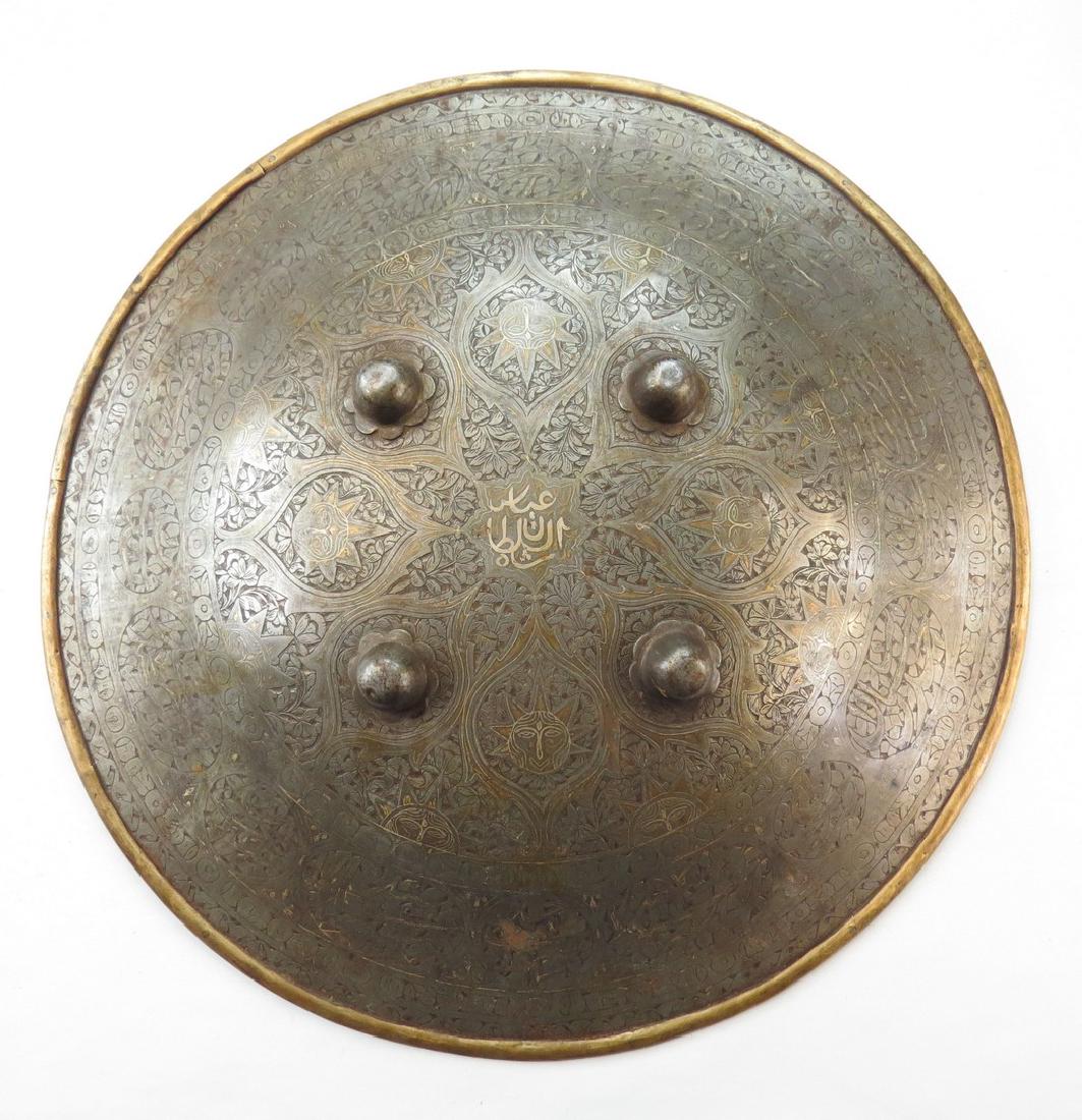 A PERSIAN SIPAR SHIELD: Qajar Dynasty, of steel with rolled brass rim, elaborately chiseled overall with well-detailed flowering vinework and anthropomorphized suns, with broad border composed of Arabic calligraphy cartouche