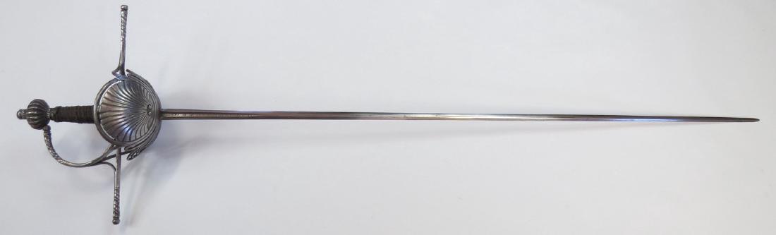 A SPANISH RAPIER SWORD: The elegant steel guard chiseled with scallop shells beneath pierced, arched rims. The guard of round section with long quillons and knucklebow with turned wrenched and beaded terminals. The engraved 