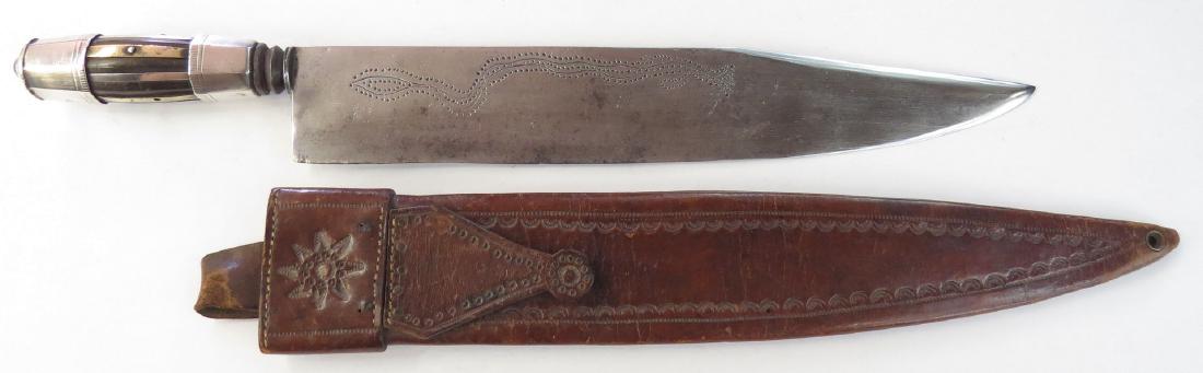 A PHILIPPINES KATIPUNAN DAGGER: The hilt composed of a faceted horn grip with applied brass strips and silver mounts. The massive blade with clipped tip and engraved motifs. In its tooled leather sheath. C. 1900. Light wear. Overall