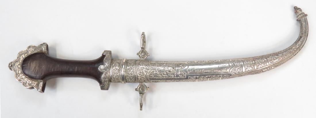 A MOROCCAN KOUMIYYA DAGGER: A fine example, the elaborately crested pommel, ferrule and scabbard wrought entirely of silver and engraved overall, with curved, single-edged blade and wooden grip. Latter 19th century. Overall leng