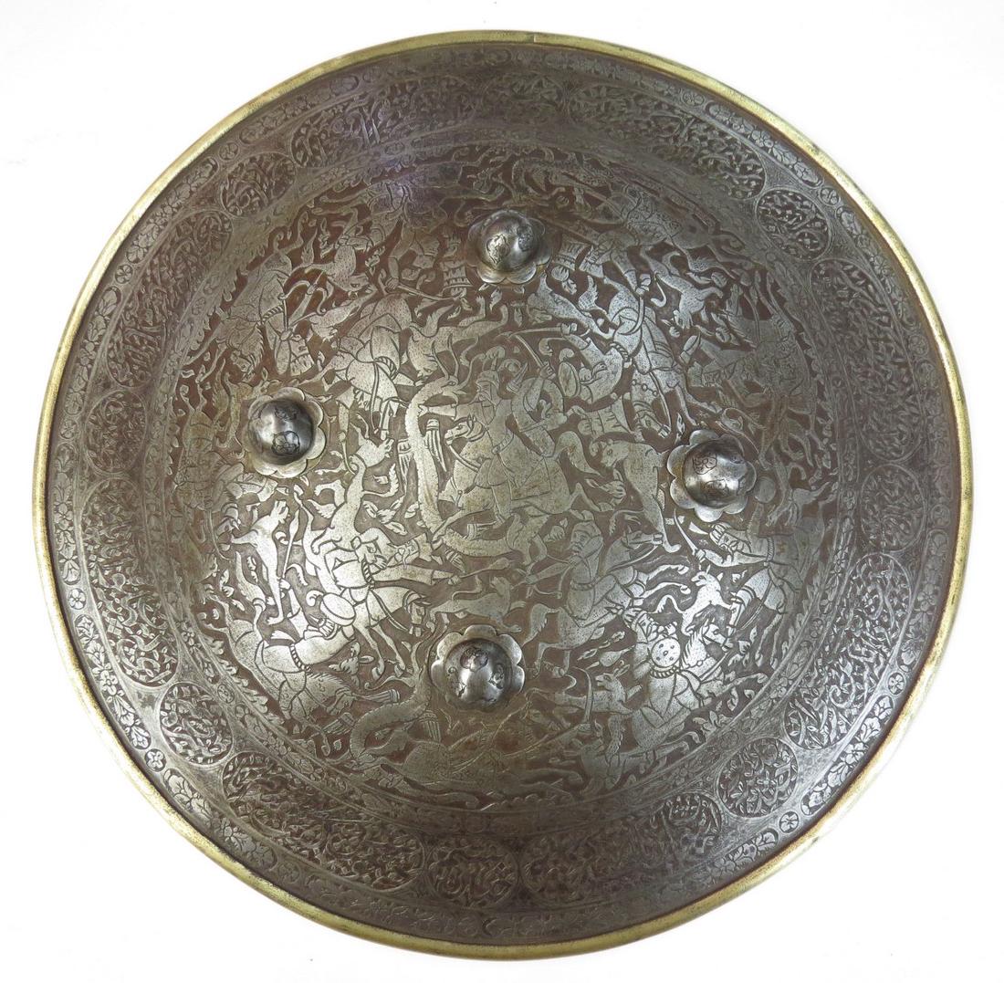 A PERSIAN SIPAR SHIELD: A rarely encountered Qajar Dynasty shield, wrought of thick steel for use against firearms. Elaborately chiseled overall with finely detailed nobles hunting and doing battle as well as a hero fighting