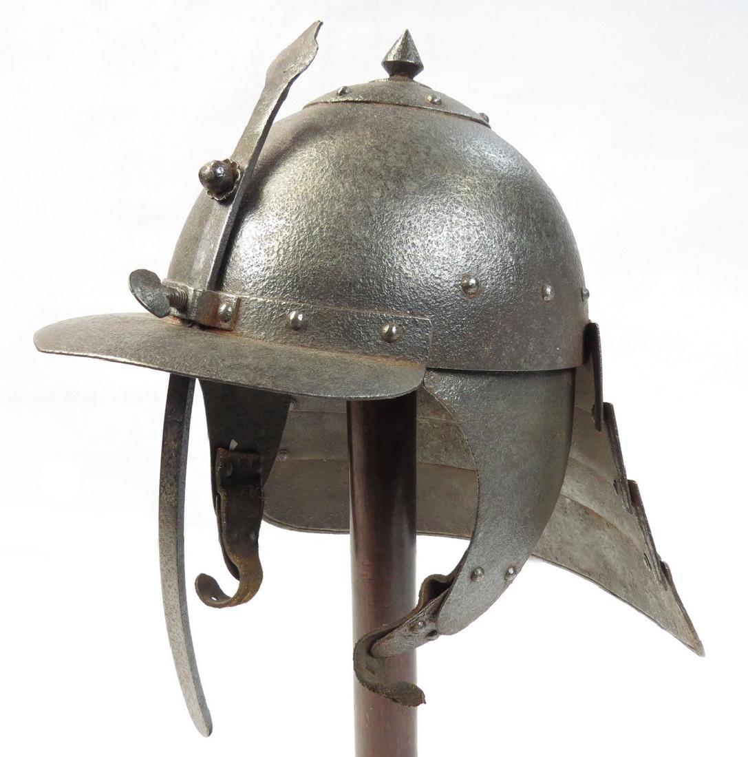 AN EASTERN EUROPEAN LOBSTERTAIL BURGONET HELMET: An officerâ€™s helmet showing quality construction throughout. The bowl wrought in one piece, the applied domed finial with spike. The separately-applied peak with sliding nasal with applied, pet