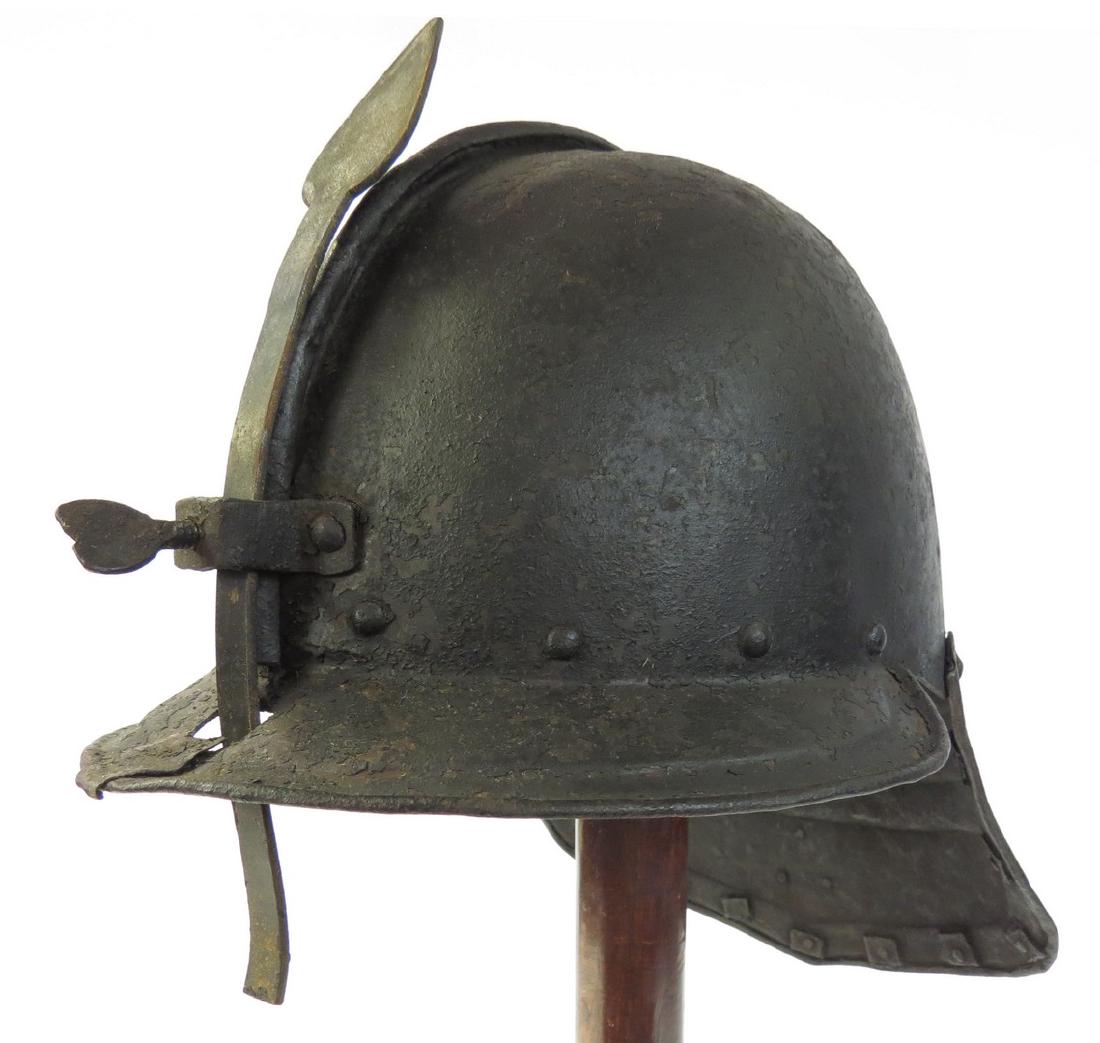 A RARE ENGLISH CIVIL WAR HELMET: A scarce type produced by English armorers during the Civil Wars, rather than imported as most were. Composed of a two-piece skull with ribbed comb and applied peak and adjustable nasal with set-screw