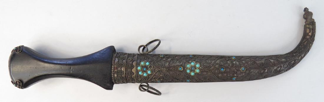 A MOROCCAN KOUMIYYA DAGGER: The grip with flared pommel and curved blade, in its matching filigreed scabbard. Embellished overall. 20th century. Minor wear. Overall length 37.6 cm. Condition II