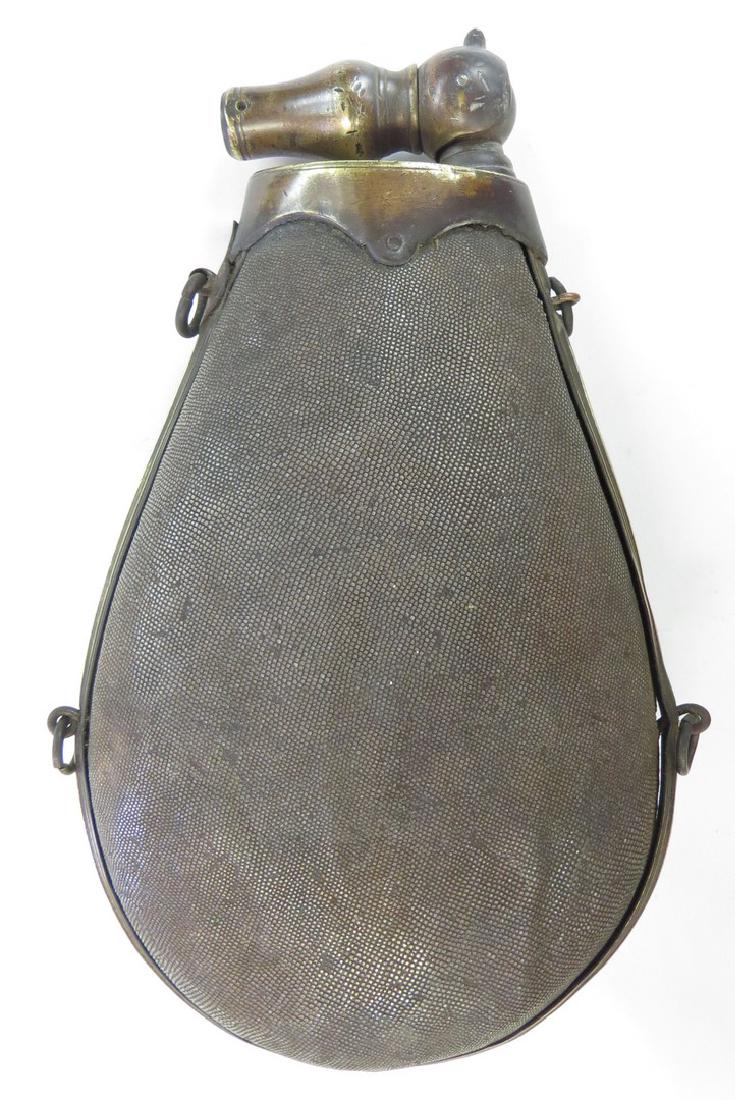 A RARE EASTERN EUROPEAN POWDER FLASK: Polish or Hungarian, the large wooden body of oval form, covered entirely in sharkskin, with profiled brass mounts and folding spout. 19th century. Worn. Overall height 24 cm. Condition III