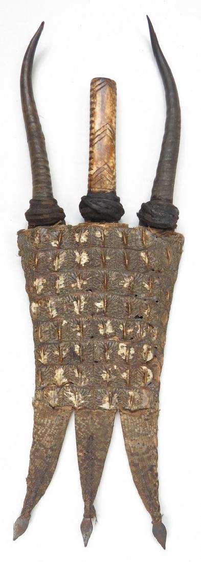 A SUDANESE TRIPLE DAGGER: Mounted and decorated en suite, with one straight and two curved blades, two with eland horn grips, the center with bone grip. The blades with stamped decorations. In their crocodile skin scabbard wit