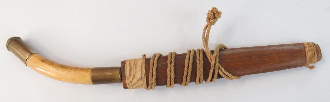 AN INDIAN DAGGER: The curved elephant grip with brass mounts, with a glass gem set in the pommel. The single-edged blade retains its cord-bound hardwood scabbard. Latter 19th century. Overall length 23.5 cm. Condition 