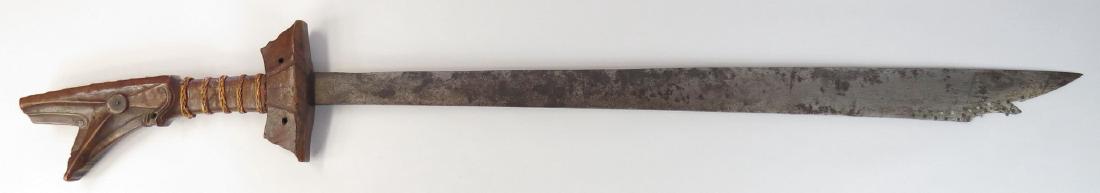 A MORO KAMPILAN SWORD: The carved hilt of figured hardwood, grip with woven rattan bands. The handwrought blade with pierced and profiled tip. Early 20th century. Blade toned and lightly pitted. Overall length 98 cm. Condit