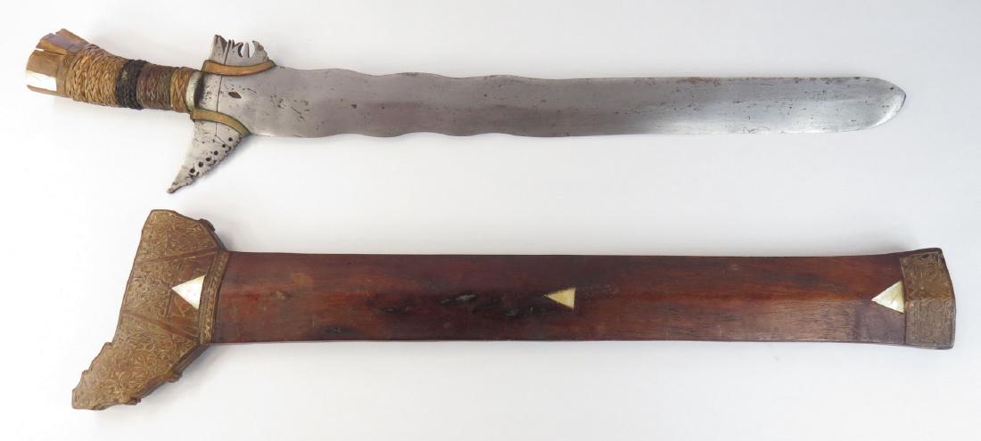 A MORO KRIS SWORD: The wooden hilt with cord and rattan-wrapped grip, flared pommel with mother of pearl inlays. The double-edged blade with separately-applied ganga and brass baca-bacas, showing evidence of layered for