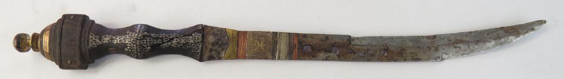 A TUAREG DAGGER: The hardwood grip profiled and inlaid with silver. The curved, pierced blade set with engraved iron, silver, brass and copper plaques. 20th century. Blade well worn. Overall length 35 cm. Condition II
