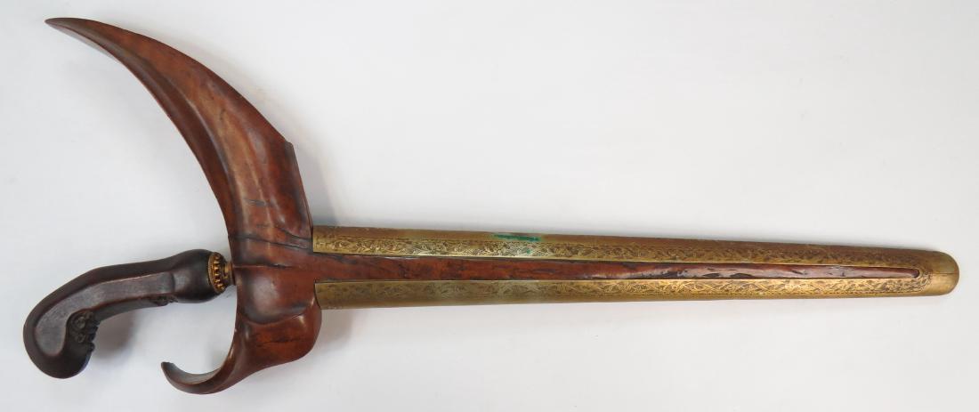 AN INDONESIAN KRIS SWORD: The exotic hardwood grip with scrolled pommel, with brass mendak, the straight, double-edged blade forged of pamor damascus steel. In its wooden scabbard with carved wrangka, the pendok wrought of bra