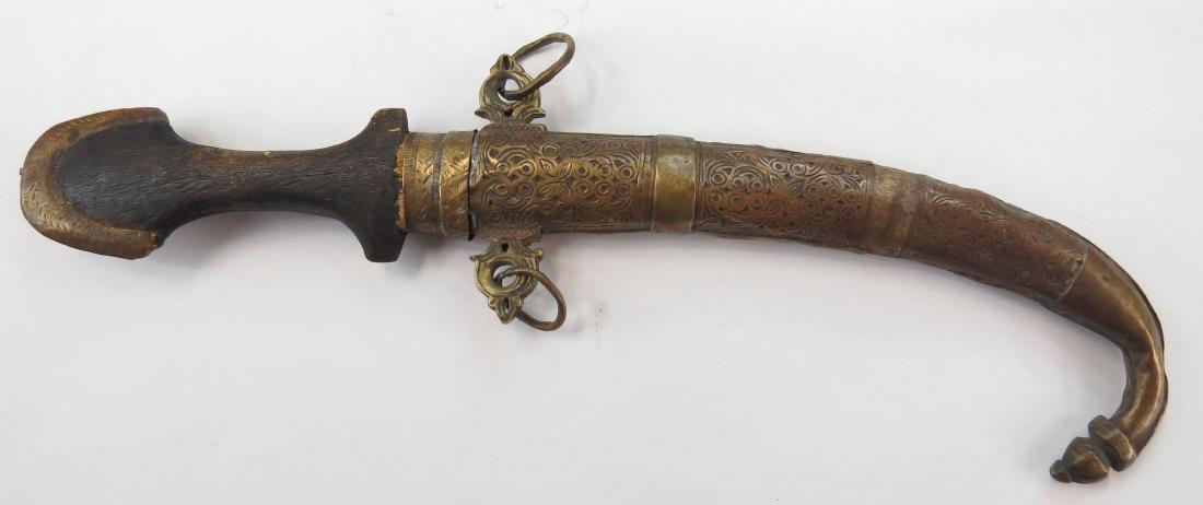 A MOROCCAN KOUMIYYA DAGGER: Mounted in engraved brass, with flared pommel and curved blade, in its matching scabbard. 19th century. Well worn. Overall length 40cm. Condition IV