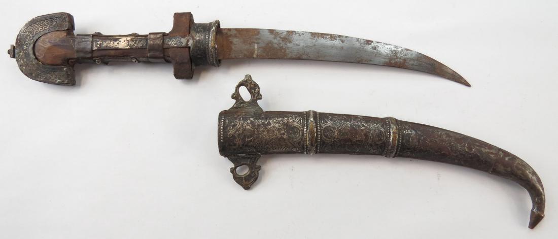 A MOROCCAN KOUMIYYA DAGGER: An older example, mounted in engraved silver, with flared pommel and curved blade, in its matching scabbard. 19th century. Well worn, with losses. Overall length 42 cm. Condition IV