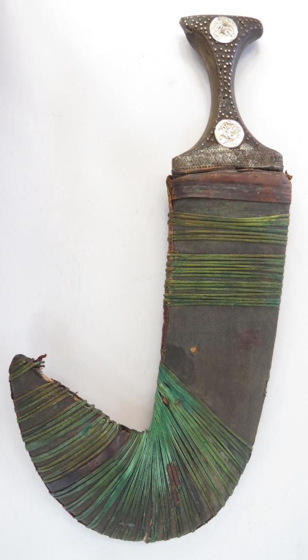 AN ARAB KHANJAR DAGGER: With horn grip and broad, curved blade with central ridge. In its leather-covered scabbard. 20th century. Worn, grip shipped. Overall length 34cm. Condition IV