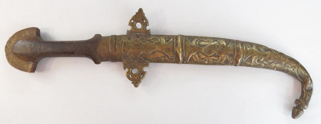 A MOROCCAN KOUMIYYA DAGGER: Mounted in engraved brass, with flared pommel and curved blade, in its matching scabbard. 19th century. Well worn. Overall length 43cm. Condition IV