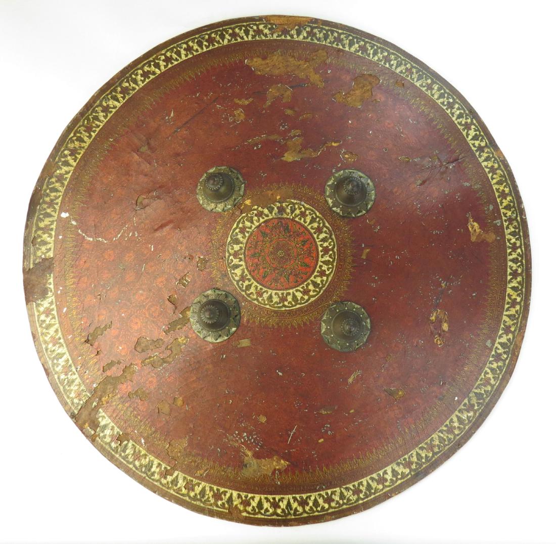 AN INDIAN DHAL SHIELD: Rajput work, a large example, circular, formed of thick hide in slightly domed form and lacquered a deep scarlet overall, with flowering vines and gold-lined cream borders with green and red vinework 