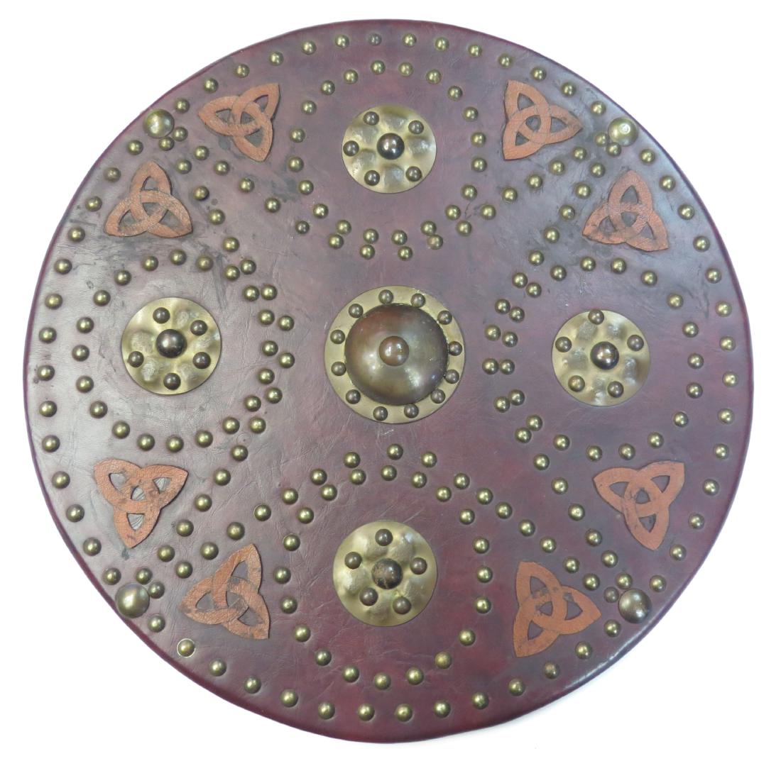 A SCOTTISH TARGE SHIELD: Of characteristic circular form, the wooden core bound in leather, the obverse elaborately embellished with brass mounts and complex geometrical brass studded motifs and leather appliques. the reverse
