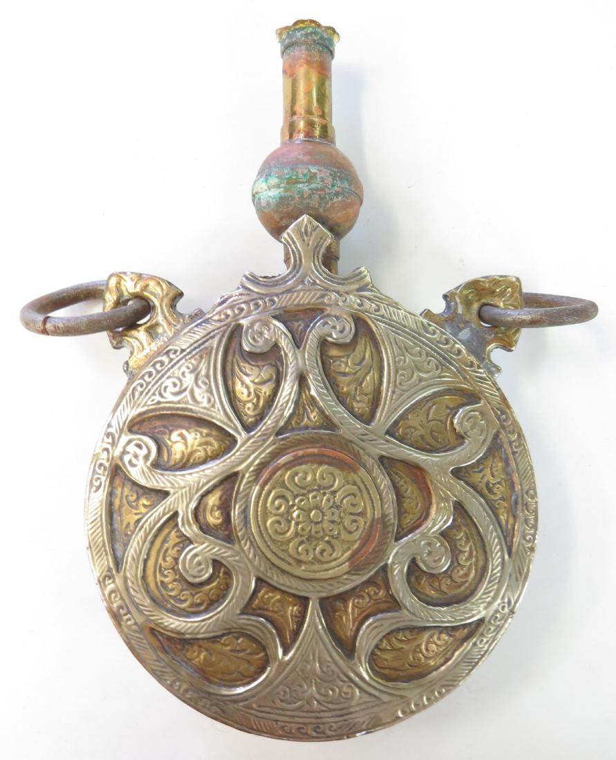 A MOROCCAN POWDER FLASK: A fine example, wrought of brass with pierced and engraved silver decoration. Latter 19th century. Wear to spout. Overall length 22.5cm. Condition III