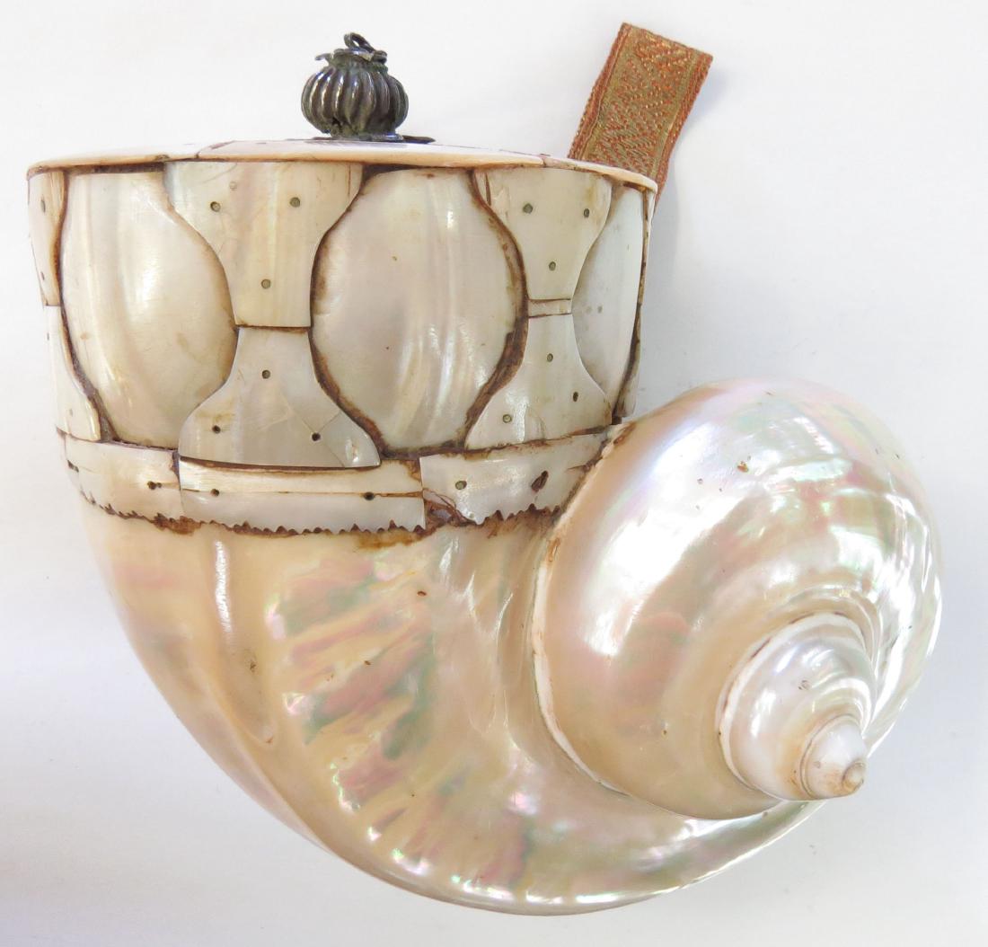 AN INDIAN BARUTDAN POWDERHORN: The body formed of a large, polished sea snail shell, the upper section formed of additional profiled shell plaques. The spout and cap of silver. Retains its embroidered suspension band. 17th-18th cen