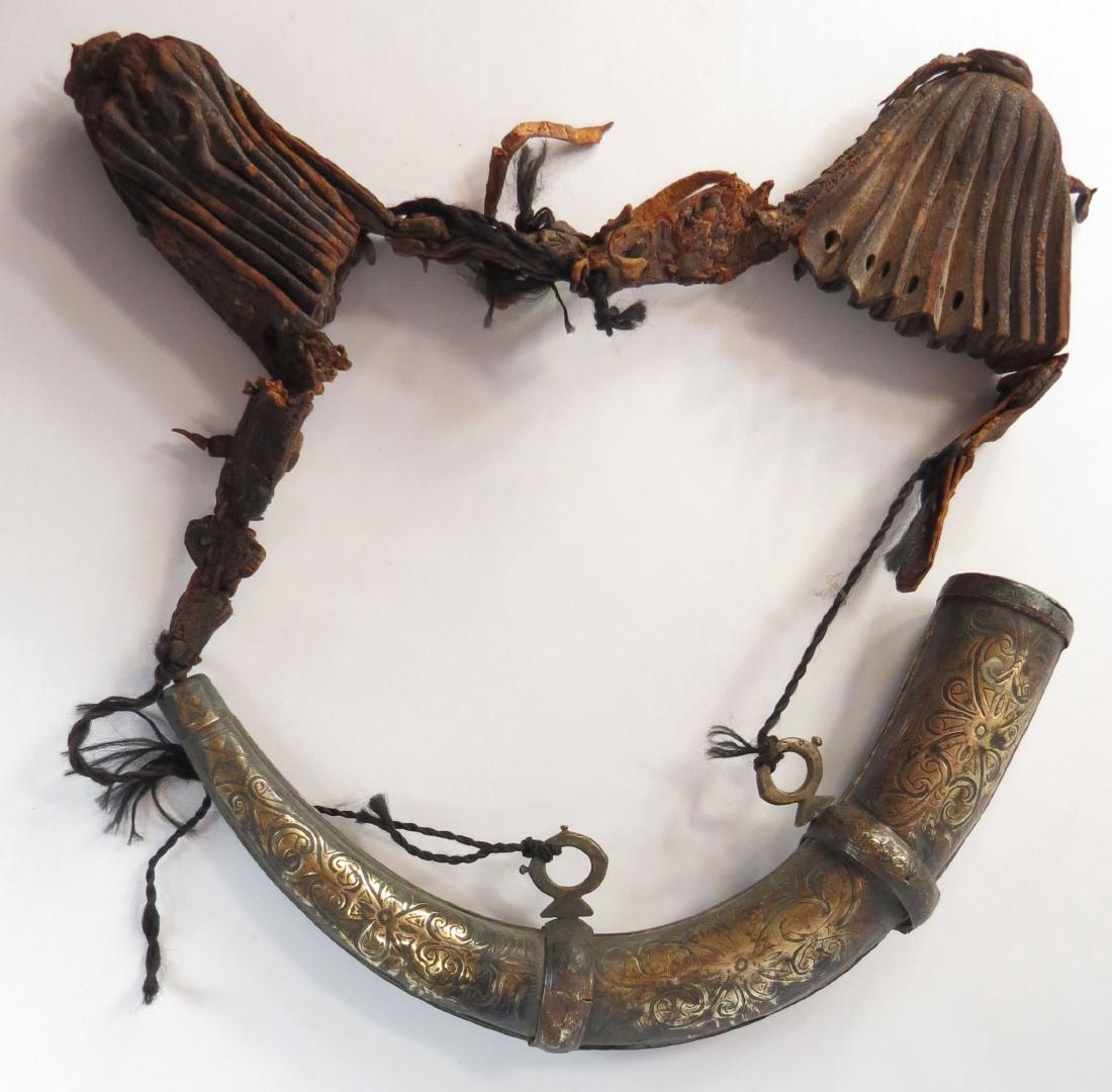 A MOROCCAN POWDERHORN AND BALL BAGS: Covered in brass and elaborately engraved overall with characteristic vinework, retains its plaited cord with a rare pair of pleated leather ball bags intact. 19th century. Worn. Overall length 32cm.