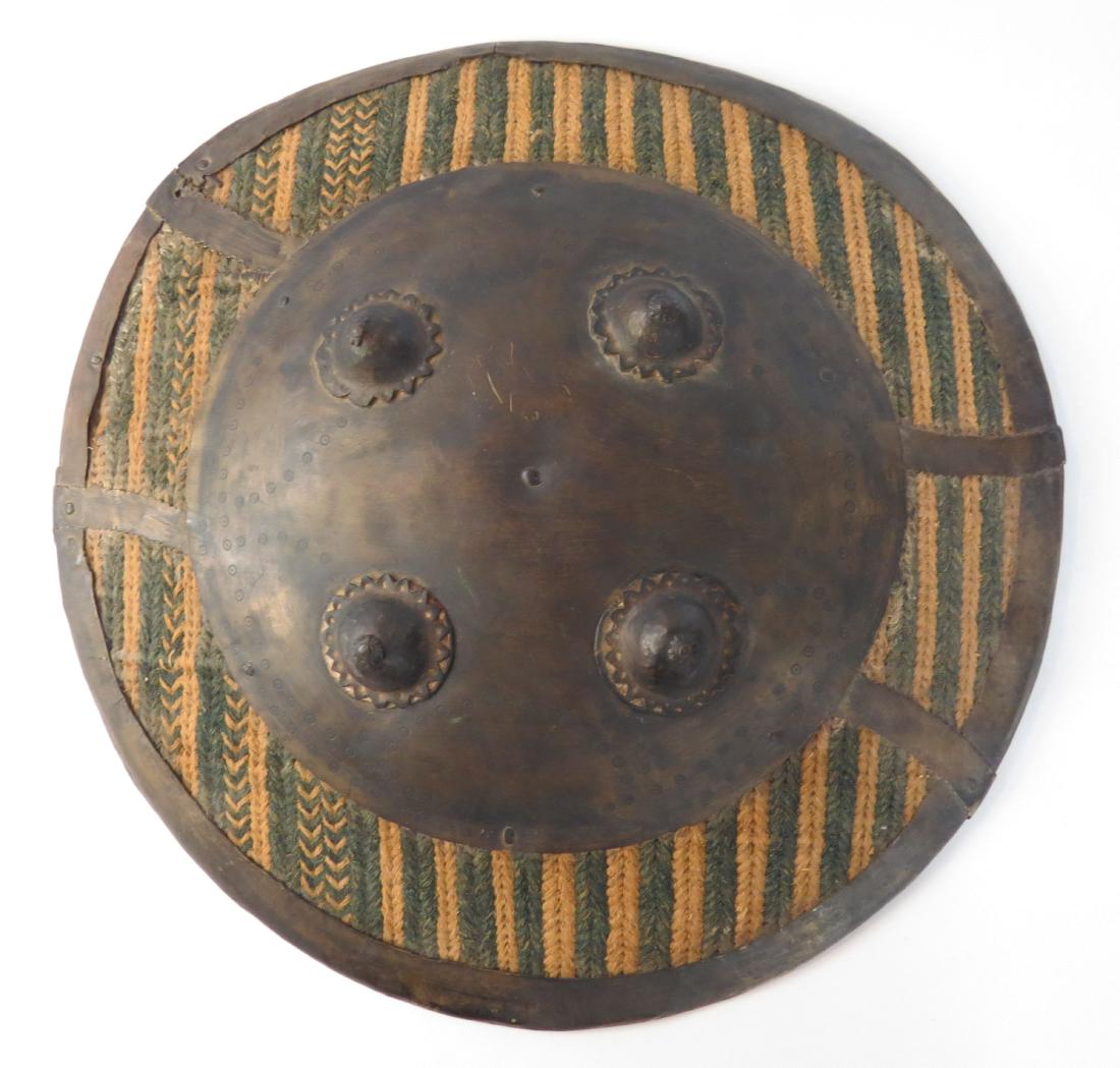 AN AFGHAN SIPAR SHIELD: Lightly-domed and composed of thick cording woven onto a metallic weft in yellow with prominent geometrical designs in blue, with iron rim, four bosses and a large circular reinforcing plate to observ
