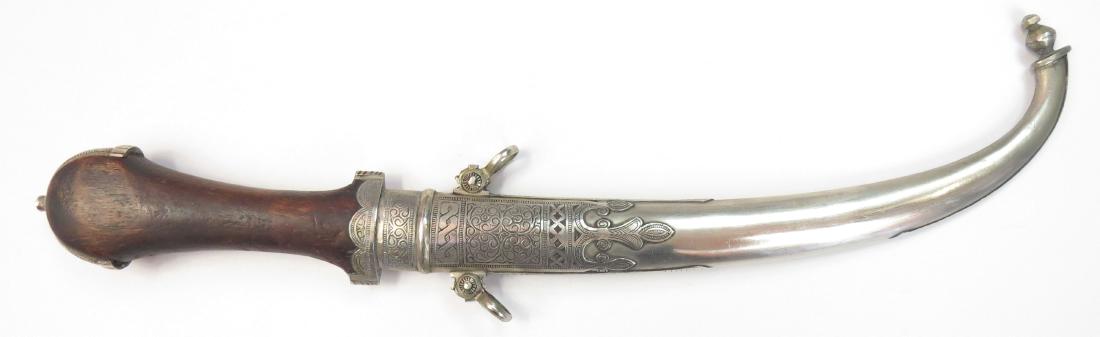 A MOROCCAN KOUMIYYA DAGGER: A massive example, the wooden grip with pierced and figured mounts. Curved blade. In its matching scabbard. 20th century. Overall length 38.5cm. Condition II