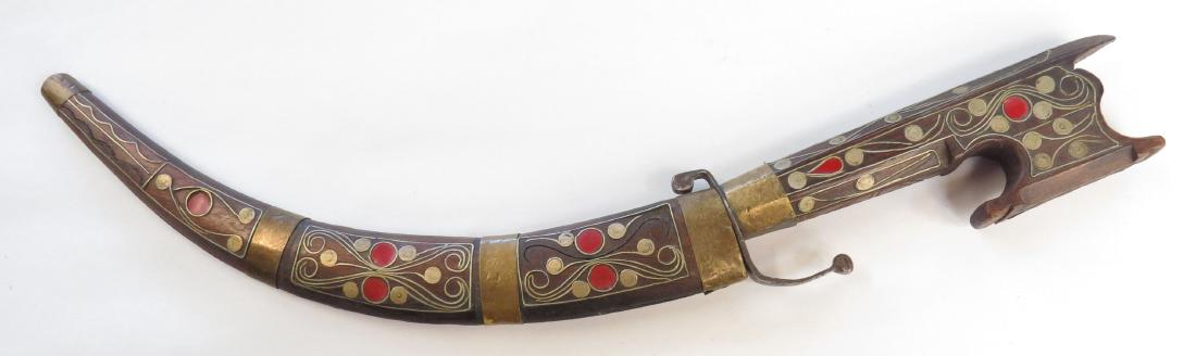 AN ALGERIAN NIMCHA DAGGER: The wooden mounts elaborately inlaid and set with brass bands. With characteristic scrolled and hooked pommel and recurved guard. The curved blade with engraved motifs. 20th century. Minor losses. Ove