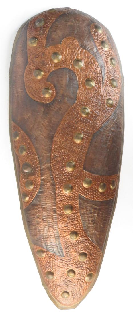 AN ARTS & CRAFTS ERA SHIELD: Of hammered copper and brass. Early 20th century. Light wear. Overall length 61.3cm. Condition III