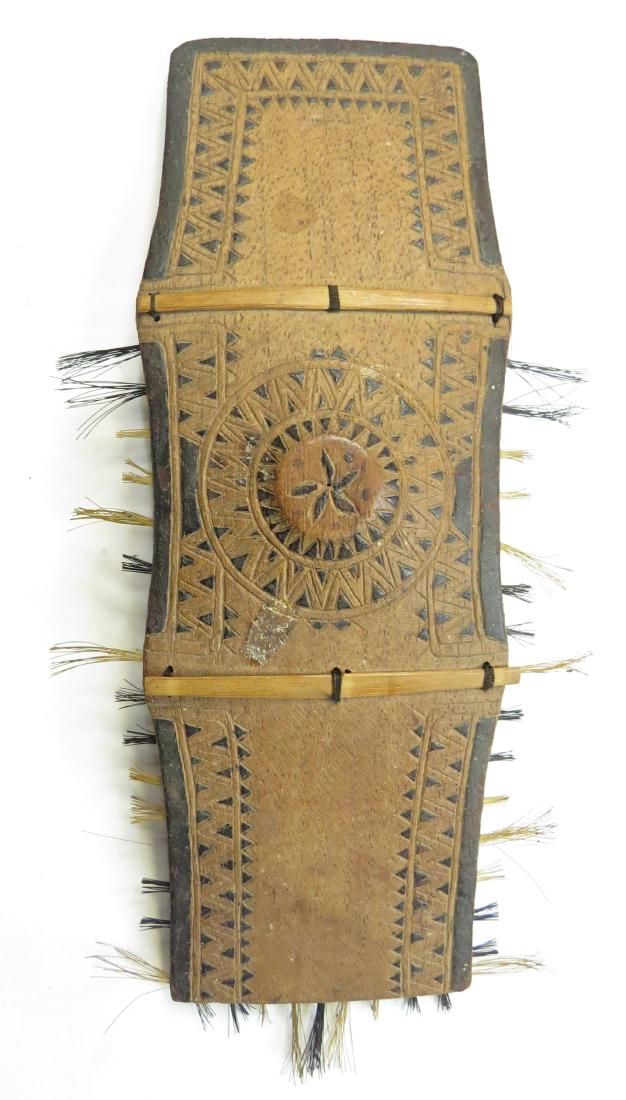 A MINIATURE BAGOBO SHIELD: Superbly carved, with fine details, stained and set with hair along the periphery. Latter 19th c. Light wear, rubbing. Miniature weapons were popular with American soldiers returning home from the Phi