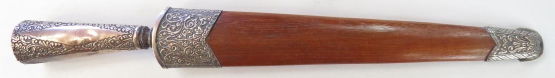 AN INDONESIAN TOMBAK SPEARHEAD: The head handwrought, showing evidence of pamor construction, with finely engraved silver socket. In its polished hardwood sheath with silver mounts en suite with the socket. 19th century. Light wear.