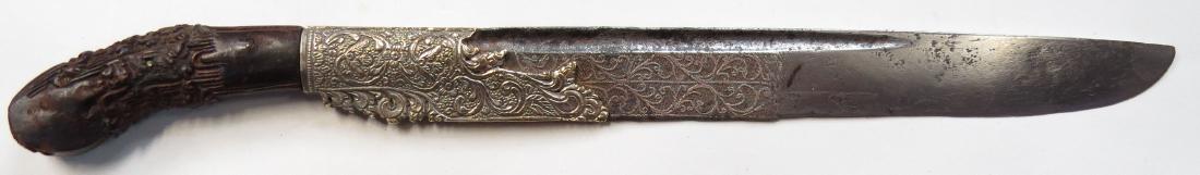 A SRI LANKAN PIHA KAETTA DAGGER: Of characteristic form, with intricately-carved ebony grip. The silver forte deeply embossed and engraved in characteristic motifs, the heavy, single-edged blade elaborately inlaid with silver vine mo