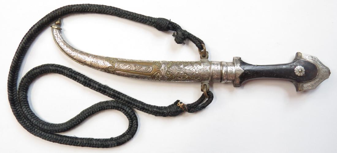 A MOROCCAN KOUMIYYA DAGGER: A fine example, the elaborately crested pommel and ferrule of silver, the scabbard wrought of silver and brass, finely engraved overall, with curved, single-edged blade and wooden grip. Retains it wov