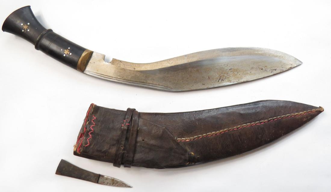 A NEPALESE KUKRIE DAGGER: The profiled horn grip with brass mounts, the thick, sharp blade with characteristic choil and raised, chamfered cutting edge. In its leather- covered wooden scabbard with by-knife. 20th century. Over