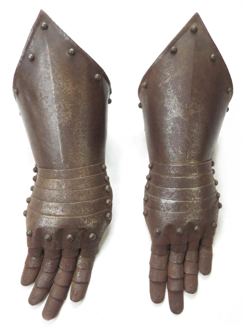 A PAIR OF ARMOR GAUNTLETS: English work, the pointed cuffs with studded, rolled and roped borders. The lames articulated and embossed at the knuckles, fingers intact. First quarter of the 17th century. Worn, rusted, thumbs lack