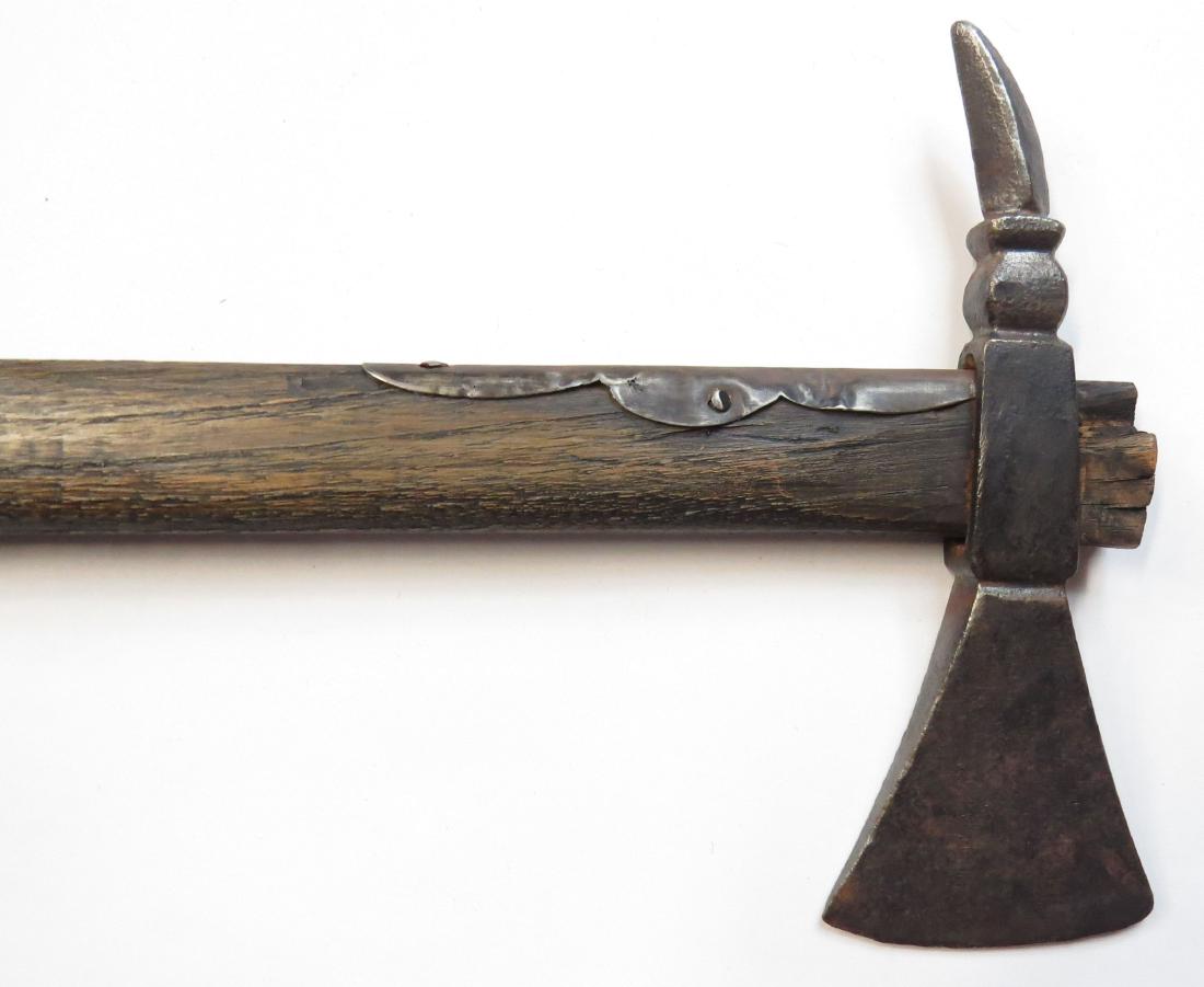 A HUNGARIAN FOKOS AXE: An older example, the massive steel head with spike pein. On its characteristically long hardwood haft with iron reinforce. 19th century. Well worn. Overall length 70.5cm. Condition II