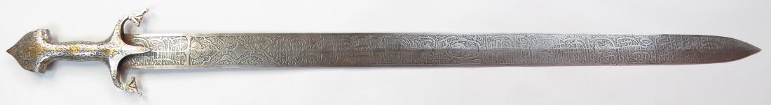 A PERSIAN BROADSWORD: Qajar era, the steel hilt with trefoil pommel and guard of characteristic form displaying curled quillons with monster head terminals, and elaborately inlaid in gold and silver overall. The blade stra