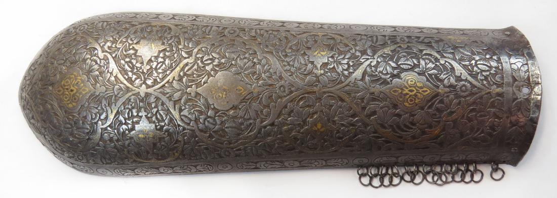 A PERSIAN BAZUBAND ARMGUARD ARMOR: Early Qajar Dynasty, raised from a single plate and finely chiseled overall in flowering vinework with gold embellishments. Early 19th century. Overall length 30.2cm. Condition II