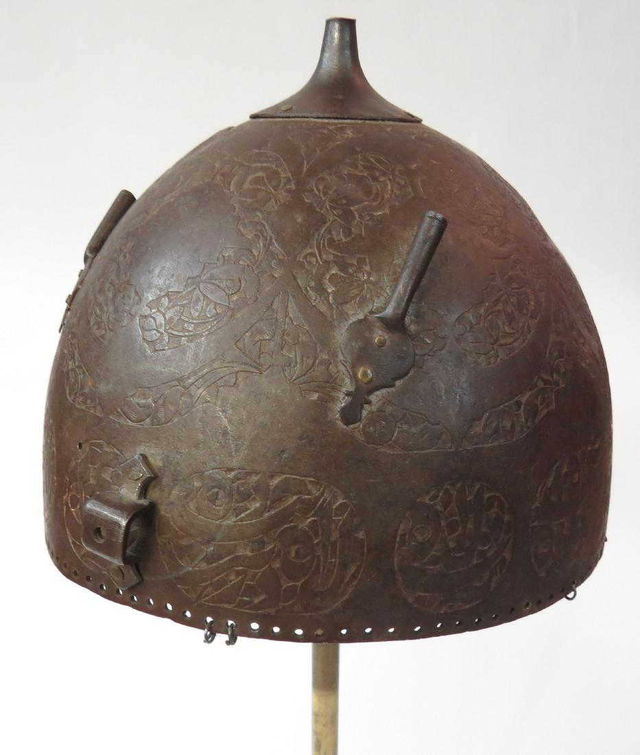 A PERSIAN KULAH KHUD HELMET: Qajar Dynasty, of characteristic hemispherical form with russet finish, embellished with engraved bands of spiral flowering vines top spike, the broad borders containing Arabic inscriptions. Plume tub