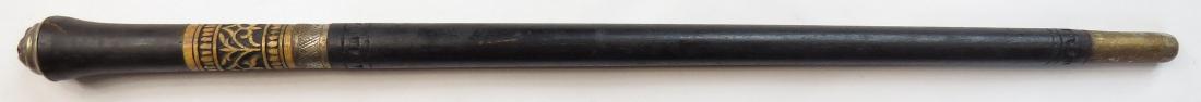 A CONTINENTAL SWAGGER STICK: Black-lacquered overall, with flared grip terminating in a brass lions head, the ferrule of carved bone with brass ring, with a robust single-edged blade. In its fitted haft with tapered tip. Latter 1