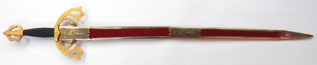 A TIZONA TOLEDO SWORD: In the style of the sword of El Cid, with cord-wrapped grip, the mounts elaborately modeled and gilded. The long, straight, double-edged blade etched and gilded. In its velvet scabbard with gilded and