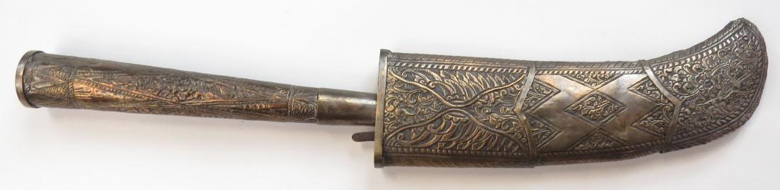 A RARE BALINESE KUDI TRANCHANG AXE: The blade with characteristic forward curve and elaborately profiled spine, elaborately inlaid in silver, the grip embossed and engraved overall. In its scabbard decorated en suite. Late 19th century.